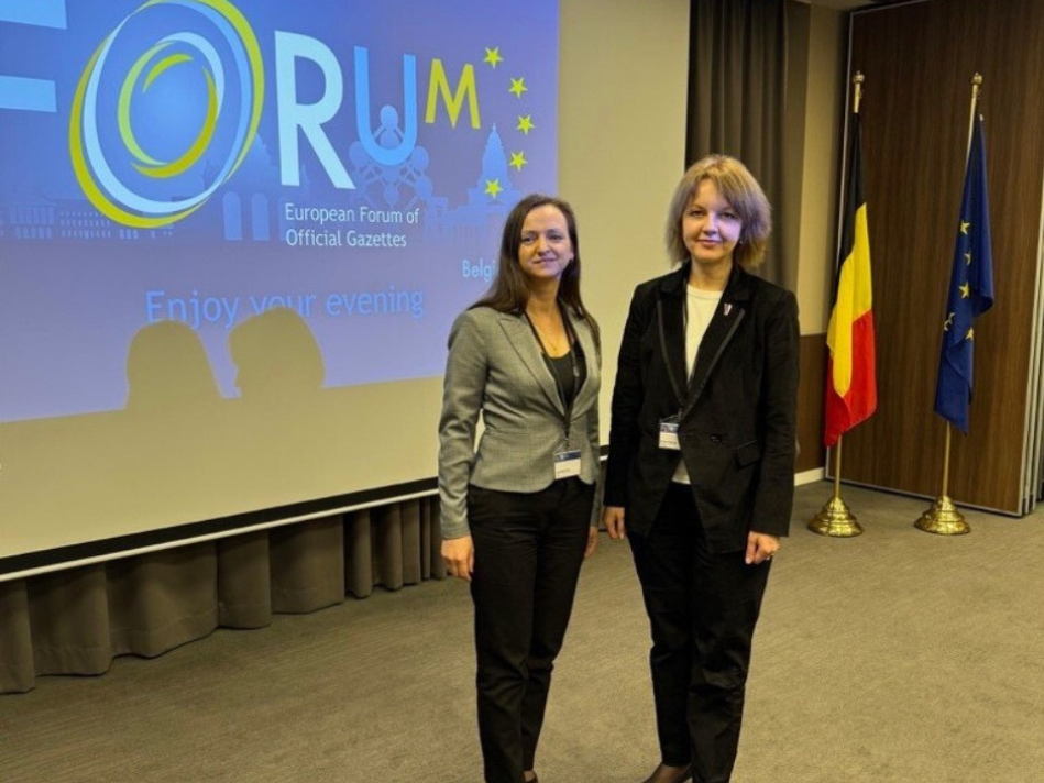 "Latvijas Vēstneša" valdes locekle un Oficiālo publikāciju departamenta Tiesību aktu sistematizācijas daļas vadītāja stāv pie ekrāna, uz kura rakstīts "European Forum of Official Gazettes". 